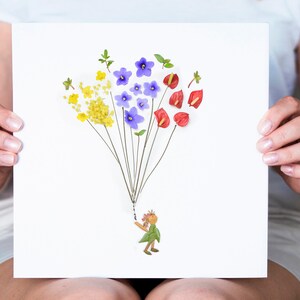 May include: A white card with a flower arrangement depicting a person holding a bunch of yellow, purple, and red flowers. The flowers are arranged to look like a hot air balloon.