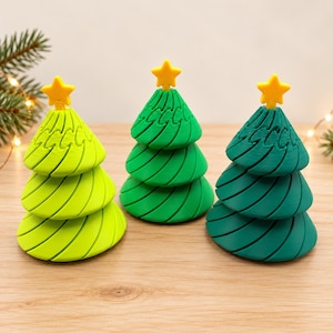 May include: Three conical Christmas tree figurines in varying shades of green, ranging from lime to dark forest green. Each tree features a spiraled, layered texture and is topped with a small, solid yellow star ornament.