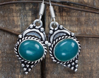Può includere: Un paio di orecchini d'argento con accenti di pietre preziose verde turchese. Gli orecchini hanno un design dettagliato con un bordo a corda attorno alle pietre.