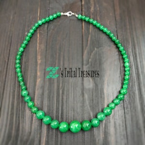 May include: A green jade bead necklace with a silver clasp. The necklace is made of round beads and has a graduated design with larger beads in the center.
