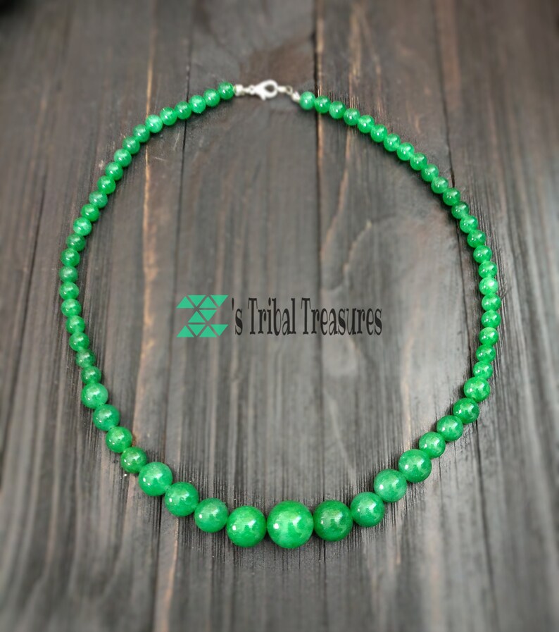 May include: A green jade bead necklace with a silver clasp. The necklace is made of round beads and has a graduated design with larger beads in the center.