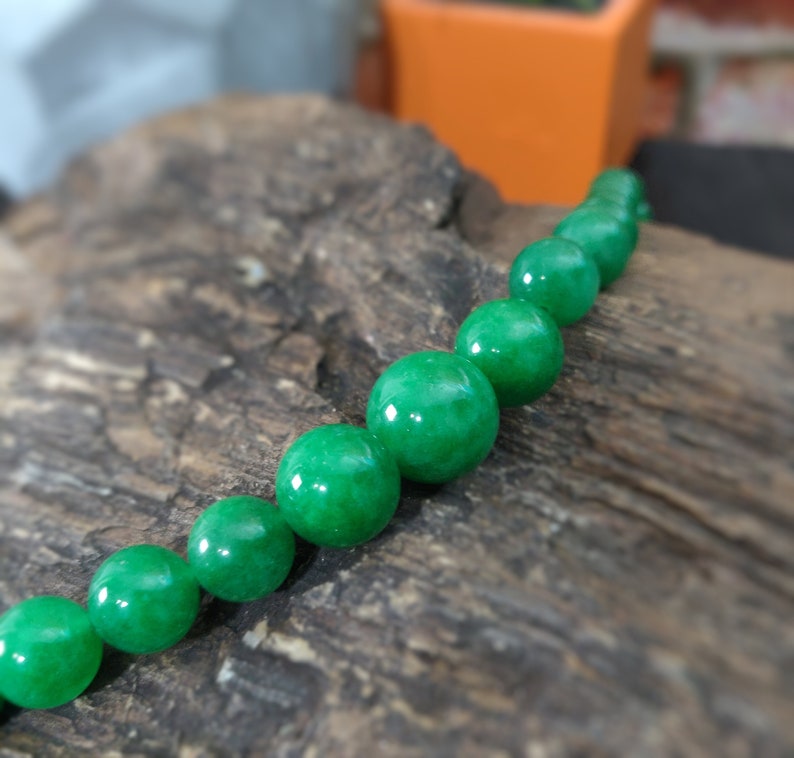 May include: A strand of round, green jade beads. The beads are smooth and polished, and they are strung on a clear thread.