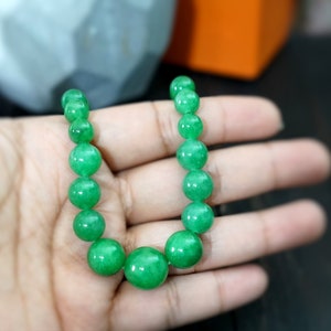 May include: A green jade bead necklace with round beads. The necklace is on a hand.