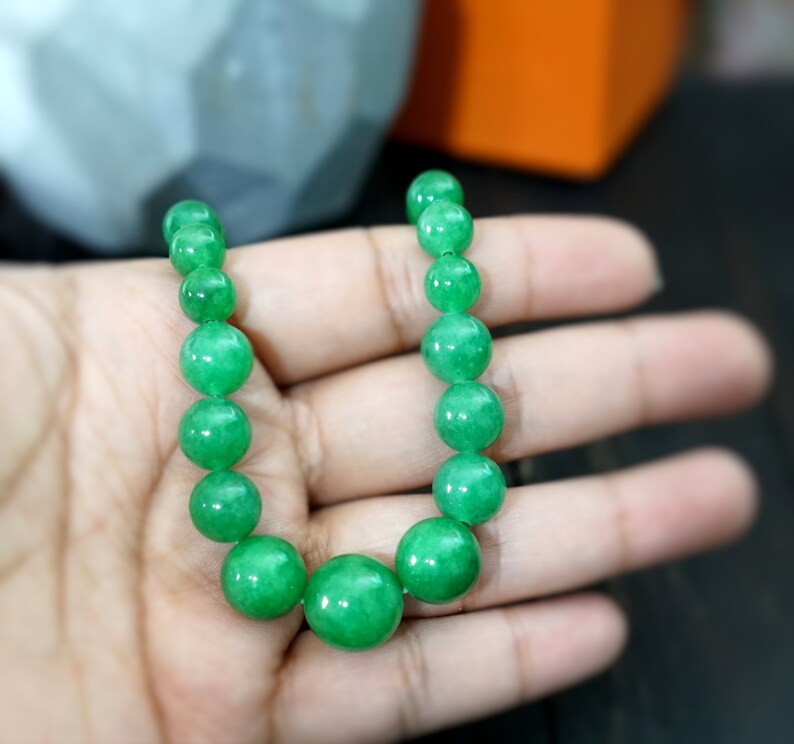 May include: A green jade bead necklace with round beads. The necklace is on a hand.