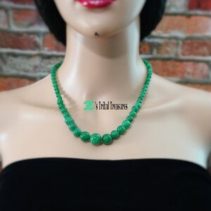 May include: A green jade bead necklace with round beads. The necklace is on a mannequin wearing a black strapless top.