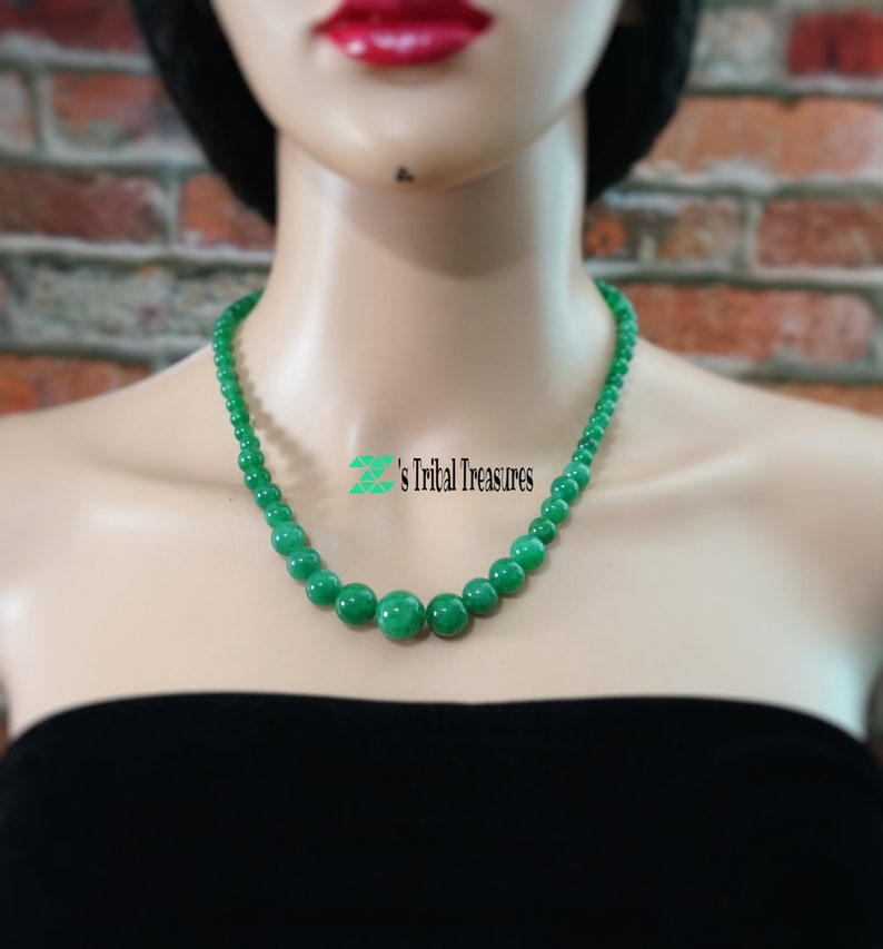 May include: A green jade bead necklace with round beads. The necklace is on a mannequin wearing a black strapless top.