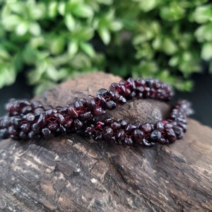 May include: A strand of dark red garnet beads strung together on a thin thread. The beads are small and irregularly shaped, giving the strand a textured look.