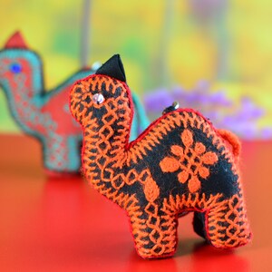 May include: Two embroidered felt camel figurines. The camel on the left is blue and green, while the camel on the right is black and orange.