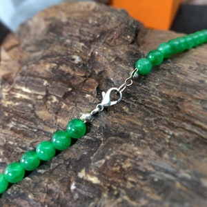 May include: A green jade bead necklace with a silver clasp. The necklace is lying on a piece of wood.