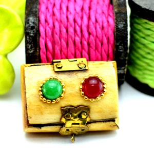 May include: A small wooden box with a brass latch and hinges. The box has two round inlays, one green and one red.