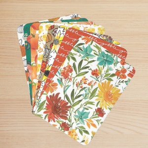 Puede incluir: Un conjunto de manteles individuales decorativos con esquinas redondeadas, con varios diseños de temática otoñal. Los patrones incluyen calabazas, girasoles y arreglos florales en tonos naranja, verde, amarillo y blanco. Algunos manteles individuales tienen la palabra "gobble".