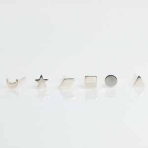 May include: A set of seven silver stud earrings featuring different geometric shapes, including a crescent moon, a star, a diamond, a rectangle, a circle, and a triangle.