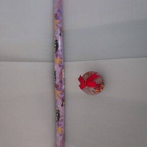 May include: A roll of purple wrapping paper featuring cartoon characters, stars, and the text "Powerpuff Girls". A clear, round ornament with a red bow is also present.