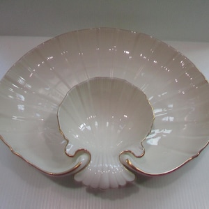 May include: A white porcelain serving dish shaped like a seashell with a smaller seashell-shaped bowl inside. The dish has a gold rim.