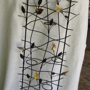 May include: A black metal wall sculpture with a design of branches and leaves. The leaves are made of gold metal and are scattered throughout the sculpture.