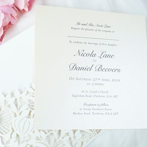 May include: Cream-coloured wedding invitation with floral detailing and pink peonies. The invitation text reads "Nicola Lane to Daniel Beevers" and includes the date, time, and location of the ceremony and reception.