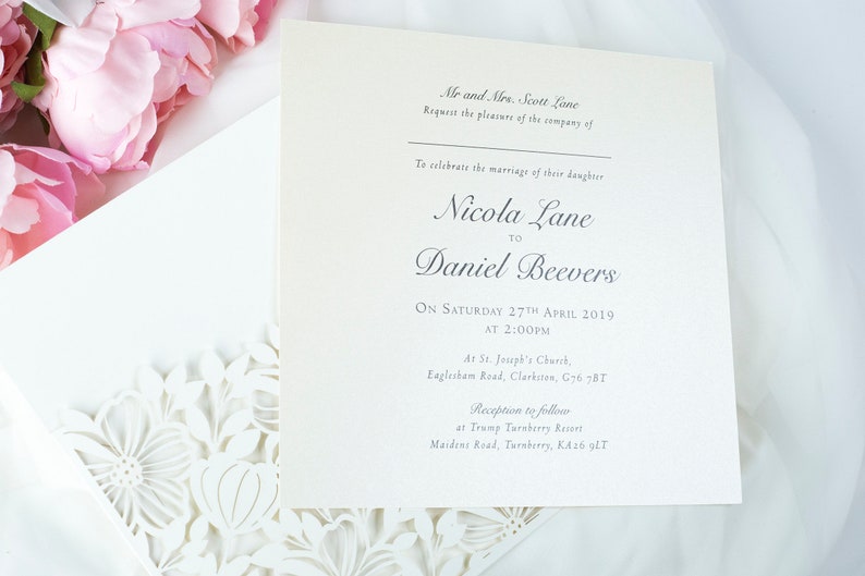 May include: Cream-coloured wedding invitation with floral detailing and pink peonies. The invitation text reads "Nicola Lane to Daniel Beevers" and includes the date, time, and location of the ceremony and reception.