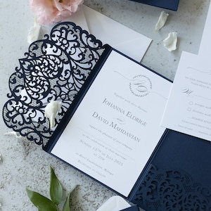 Pode incluir: Um conjunto de convites de casamento azul-marinho cortados a laser com padrões de filigrana intrincados nas capas. O encarte branco exibe o texto: Johanna Eldrige e David Mahdavian solicitam o prazer da sua companhia em 15 de julho de 2025.