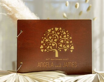May include: A brown wooden guest book with a gold tree design and hearts. The book has a date and names engraved on the front: "24th September 2027 Angela and James".
