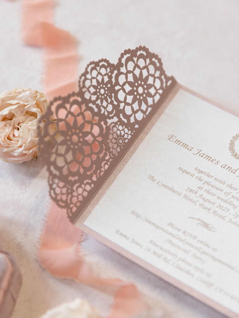 May include: A pink and white wedding invitation with a delicate lace design. The invitation features the names "Emma James and" and the date "29th August 2025".