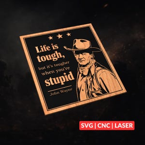 May include: A square wooden plaque featuring a black center with a laser-engraved portrait of John Wayne wearing a cowboy hat. The text reads: Life is tough, but it's tougher when you're stupid, followed by the name John Wayne and three stars.