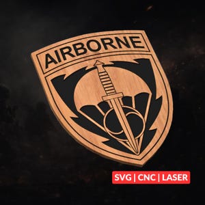 Op de afbeelding: Houten schildvormig embleem met het woord "AIRBORNE" bovenaan. Het embleem heeft een zwarte achtergrond met een parachute en een dolk. De tekst "SVG | CNC | LASER" staat onderaan.