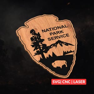 Op de afbeelding: Houten bord in de vorm van een pijl, met het logo van de National Park Service. Het logo bevat een bergketen, bomen en een bizonsilhouet, allemaal in zwart tegen een lichtbruine houtnerf achtergrond.