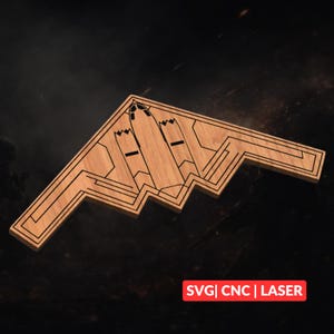 May include: A wooden B-2 Spirit stealth bomber model with intricate laser-cut details. The model is light brown with dark brown etched lines, and features the text "SVG | CNC | LASER" in a red box.