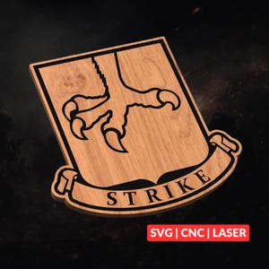 Könnte beinhalten: Holzschild mit einem schwarzen Umriss einer Vogelkralle auf einem schildförmigen Hintergrund. Das Wort "STRIKE" ist auf einem Banner darunter zu sehen. Das Schild ist aus hellem Holz gefertigt. Der Text "SVG | CNC | LASER" wird in einem roten Rechteck angezeigt.