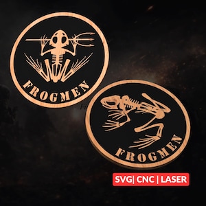 Puede incluir: Dos placas circulares de madera con fondo negro y marco de madera marrón claro. Las placas presentan un diseño de esqueleto de rana y la palabra "FROGMEN". El texto "SVG | CNC | LASER" está en la esquina inferior derecha de la imagen.