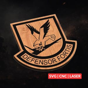 Puede incluir: Placa de madera con un emblema de águila negra y las palabras "DEFENSOR FORTIS" en un diseño curvo. La placa es de madera clara con un borde oscuro. La esquina inferior derecha tiene el texto "SVG | CNC | LASER".