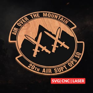 Könnte beinhalten: Holzemblem mit dem Text "AIR OVER THE MOUNTAIN" und "20TH AIR SUPT OPS SQ". Das Emblem zeigt eine Bergsilhouette und drei gekreuzte Schwerter. Der Text "SVG | CNC | LASER" befindet sich unten.