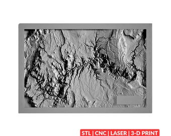 May include: A rectangular gray relief map featuring intricate topographical terrain details with deep shadows and highlights. A small rectangular blank space is located in the bottom right corner. Below the map, the text reads STL | CNC | LASER | 3-D PRINT.