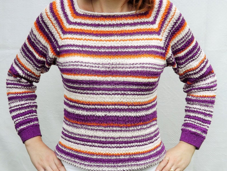Pu&ograve; includere: Un maglione in maglia a maniche lunghe con un motivo a righe orizzontali nei toni del viola, arancione brillante e bianco sporco. Il capo presenta uno scollo quadrato e polsini a coste all'estremit&agrave; di ogni manica, in filato testurizzato.