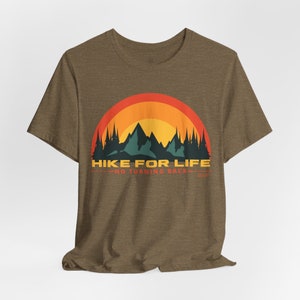 May include: Brown t-shirt with a graphic design featuring a mountain range, trees, and a sunset in shades of orange, yellow, and green. The text "HIKE FOR LIFE" and "NO TURNING BACK" are printed below the graphic.