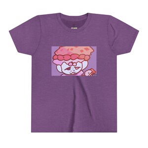 May include: Purple t-shirt featuring a cartoon character with a mushroom-shaped hat and a small red object. The graphic is set within a rectangular frame. The shirt has a crew neck and short sleeves. The image has the artist's signature in the bottom right corner.