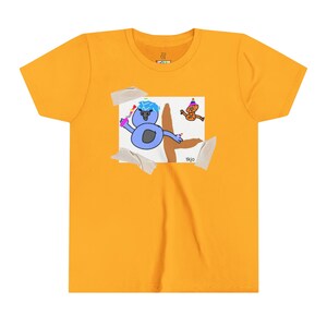 Könnte beinhalten: Senfgelbes T-Shirt mit einer verspielten Illustration einer blauen Kreatur mit Partyhut und einer braunen Figur. Das Kunstwerk ist mit Klebeband befestigt. Der Text "tkjo" ist auf dem Kunstwerk zu sehen.