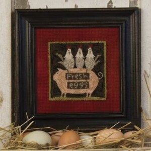 May include: A framed needlepoint design featuring a pink pig with three white chickens perched on top. The pig is holding a sign that reads "Fresh Eggs".