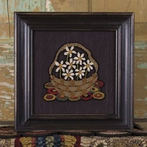 May include: A framed needlepoint artwork depicting a brown basket filled with white daisies. The basket is sitting on a brown and orange rug.