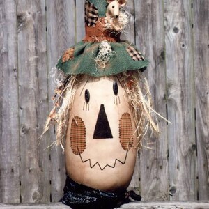 May include: A whimsical scarecrow with a green hat, brown face, and straw hair. The scarecrow is topped with a black bird and three small mice.