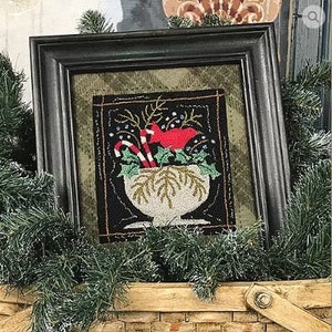 May include: A framed needlepoint design featuring a red cardinal perched in a white bowl filled with holly and candy canes. The background is black with a dark green border.
