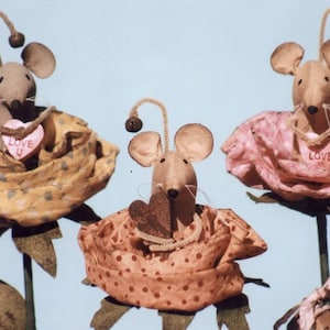 May include: Three handmade fabric mice dressed in rose-shaped outfits. Each mouse holds a heart-shaped candy with the words "Love You" printed on it. The roses are in shades of yellow, pink, and orange.