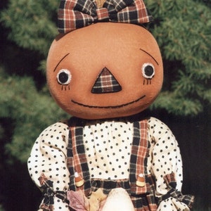 May include: A handmade pumpkin doll with a plaid bow, white polka dot dress, and plaid overalls. The doll is holding a candy corn prop.