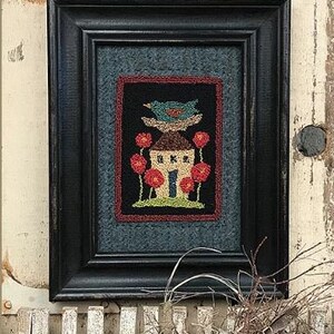 May include: A framed needlepoint artwork depicting a small house with a bird perched on the roof. The house is surrounded by red flowers and green foliage. The artwork is set against a blue background.