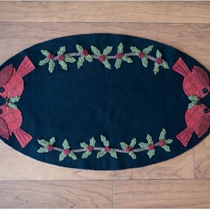 May include: A black oval wool rug with a red cardinal bird design and a green holly border. The rug is perfect for a winter or Christmas theme.