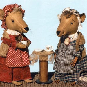 May include: Two anthropomorphic mouse dolls dressed in vintage clothing. One mouse wears a red dress with a checkered apron and holds a teacup. The other mouse wears a plaid dress and apron. A small table with teacups sits between them.