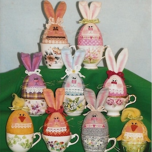 May include: Nine Easter bunny and chick figurines in teacups. The bunnies are made of fabric and have painted faces. The chicks are made of fabric and have embroidered faces. The teacups are decorated with floral patterns.