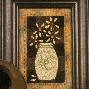 May include: Framed artwork featuring a jar of flowers. The jar is light green with the word "Love" stitched on it. The background is a dark brown checkered pattern with a tan border, all within a dark brown wooden frame.