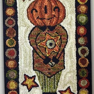 May include: A rectangular, hand-stitched rug featuring a smiling pumpkin-headed figure with a star-shaped design on its chest. The rug has a white background, a black border, and colorful floral accents. Two gold stars are at the bottom.