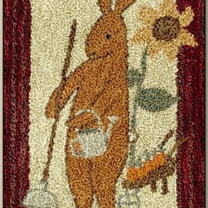May include: A brown bunny with a watering can in its pocket stands next to a wheelbarrow filled with gardening tools. A sunflower with yellow petals and a green stem is in the background. The image is a rug with a cream background and a red border.